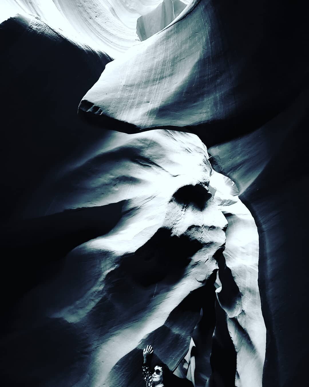 A small figure with an arm raised beneath a towering slot-canyon rock face, Antelope Canyon, Arizona
